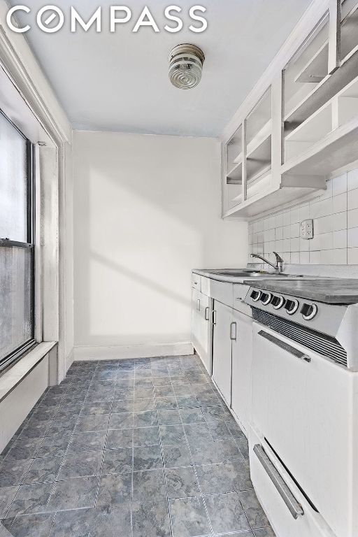 kitchen with tasteful backsplash, electric range, sink, and white cabinetry