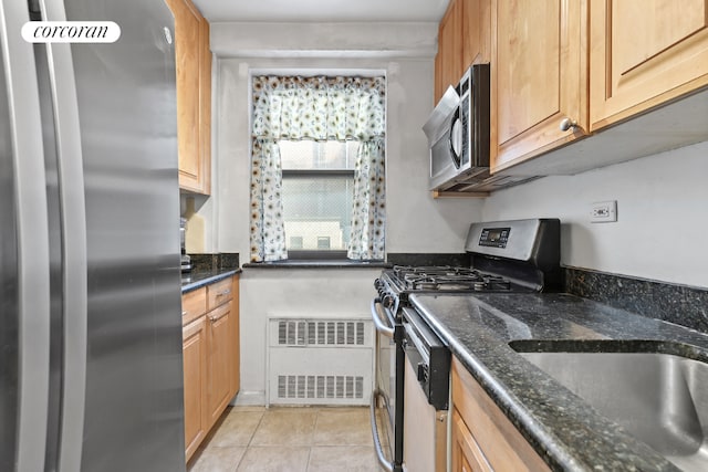 kitchen featuring light tile patterned flooring, appliances with stainless steel finishes, radiator heating unit, and dark stone countertops