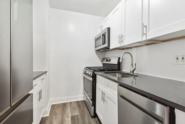 kitchen with dark countertops, appliances with stainless steel finishes, a sink, and wood finished floors