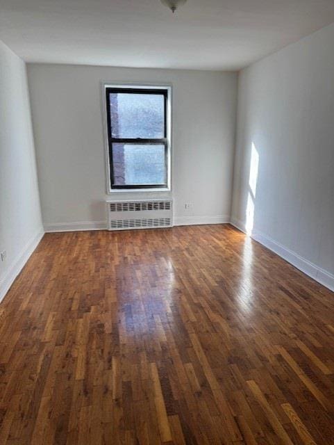 spare room with baseboards, radiator heating unit, and wood finished floors