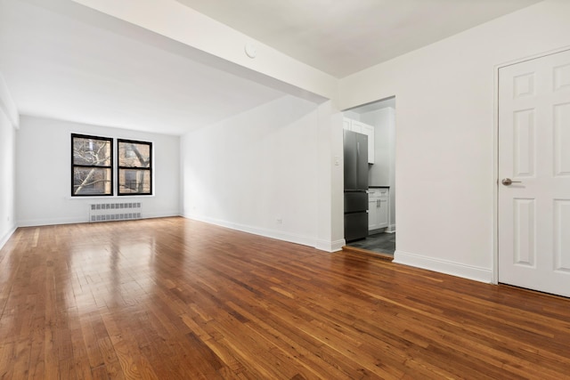 spare room with baseboards, dark wood-type flooring, and radiator