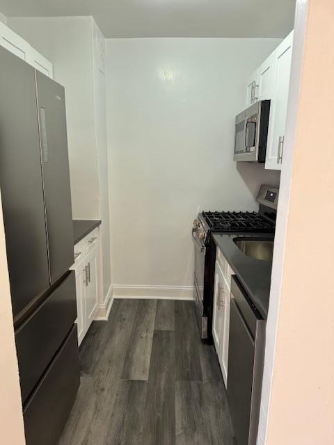 kitchen featuring dark countertops, white cabinets, stainless steel appliances, and dark wood-style flooring