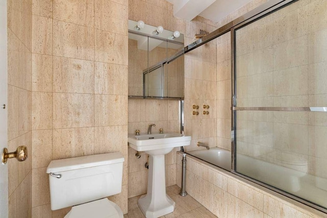 bathroom with toilet, tile patterned flooring, tile walls, and shower / bath combination with glass door