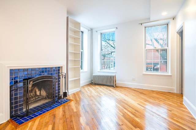 living room with a tiled fireplace, a wealth of natural light, radiator heating unit, and wood-type flooring