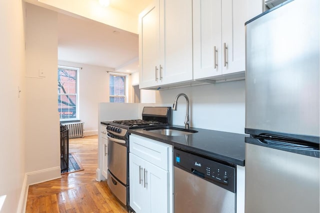 kitchen featuring white cabinetry, stainless steel appliances, sink, light wood-type flooring, and radiator heating unit