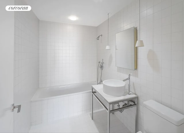 full bath with tile walls, a sink, toilet, and tiled shower / bath combo