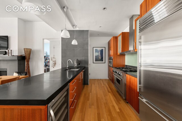 kitchen featuring sink, beverage cooler, high end appliances, wall chimney range hood, and light wood-type flooring