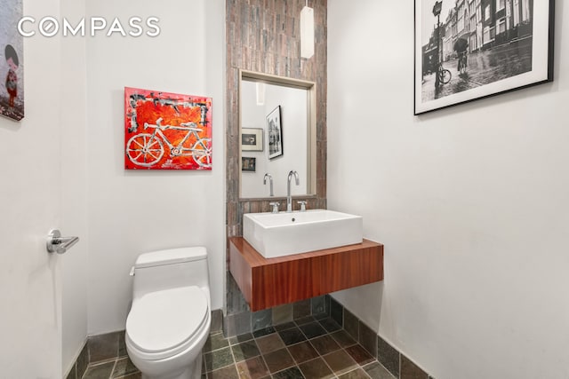 half bathroom with toilet, a sink, stone finish floor, and baseboards