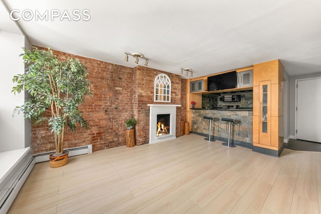 unfurnished living room with a baseboard heating unit, a warm lit fireplace, brick wall, a dry bar, and wood finished floors