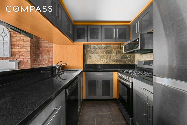 kitchen with backsplash, appliances with stainless steel finishes, glass insert cabinets, a sink, and dark tile patterned flooring