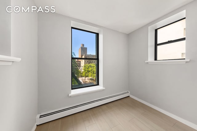 unfurnished room with baseboard heating, wood finished floors, and baseboards