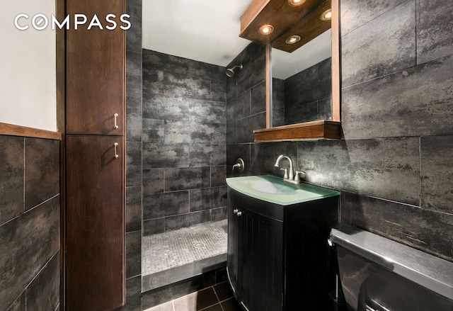 bathroom featuring a tile shower, toilet, tile walls, tile patterned floors, and vanity