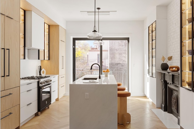 kitchen featuring visible vents, an island with sink, gas range oven, modern cabinets, and a sink