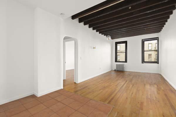 empty room featuring arched walkways, radiator heating unit, wood finished floors, beamed ceiling, and baseboards