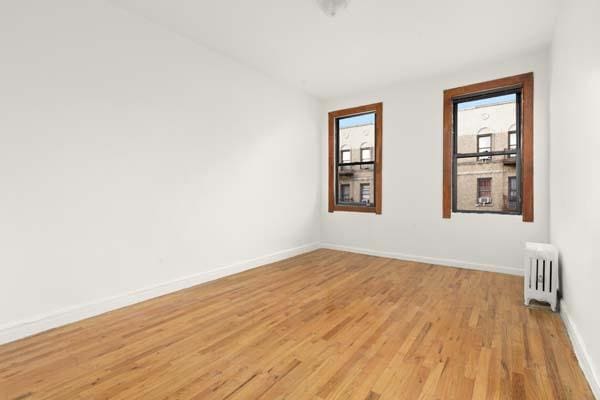 unfurnished room featuring baseboards, vaulted ceiling, light wood finished floors, and radiator heating unit