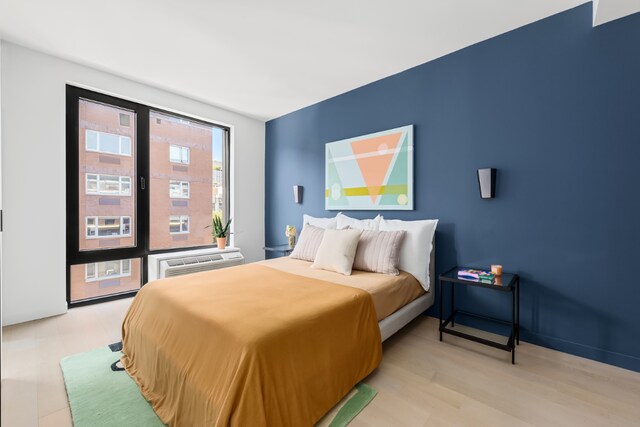 bedroom with light wood-style floors and an AC wall unit