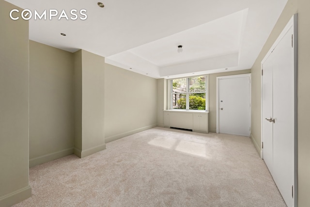 spare room featuring baseboards, a tray ceiling, and light colored carpet