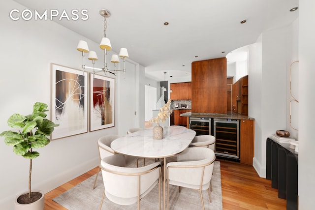 dining room featuring beverage cooler, baseboards, an inviting chandelier, and light wood-style floors