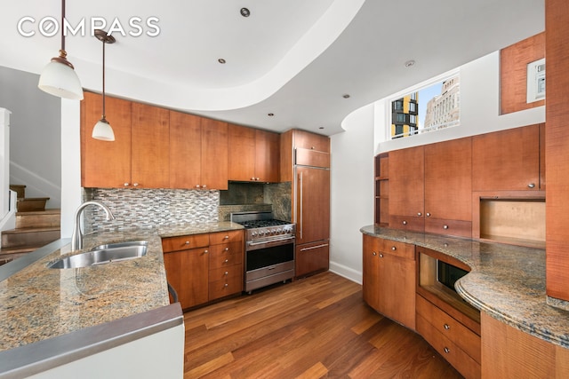 kitchen with brown cabinetry, premium appliances, dark wood-style floors, hanging light fixtures, and a sink