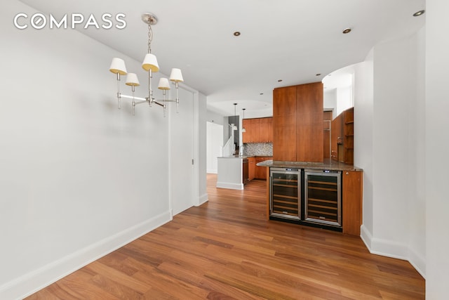 kitchen featuring brown cabinetry, wine cooler, backsplash, and wood finished floors