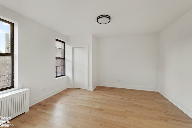 empty room with light wood finished floors, a healthy amount of sunlight, baseboards, and radiator