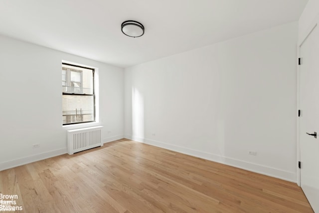 empty room with baseboards, light wood-style floors, and radiator