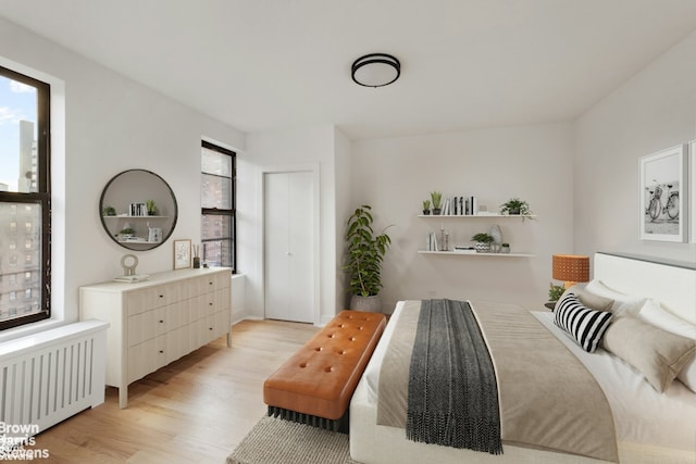 bedroom featuring multiple windows, radiator heating unit, a closet, and light wood-style floors