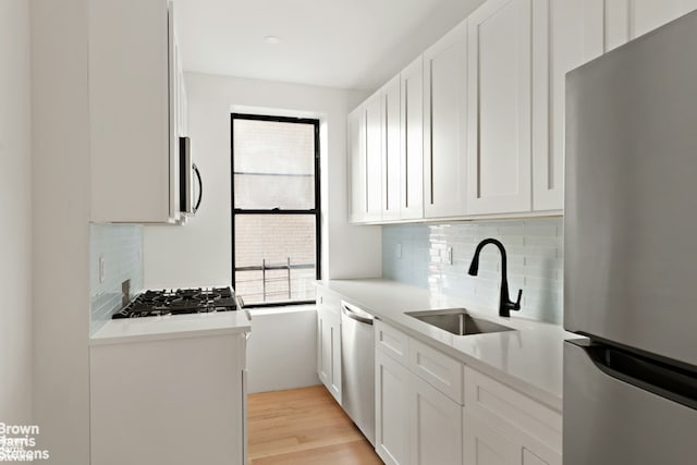 kitchen featuring stainless steel appliances, light countertops, light wood-type flooring, white cabinetry, and a sink