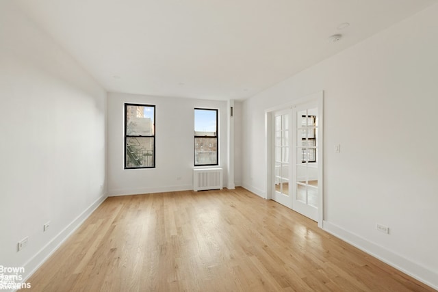 spare room with baseboards, light wood finished floors, and radiator