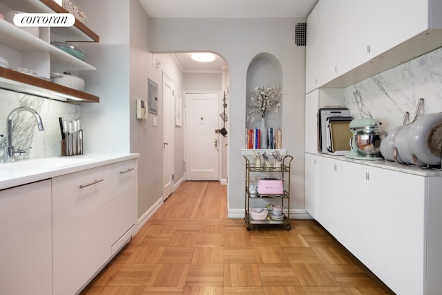 kitchen with light parquet flooring, sink, white cabinets, and decorative backsplash