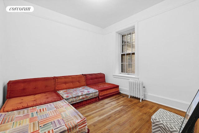 living area featuring hardwood / wood-style floors, radiator heating unit, baseboards, and visible vents