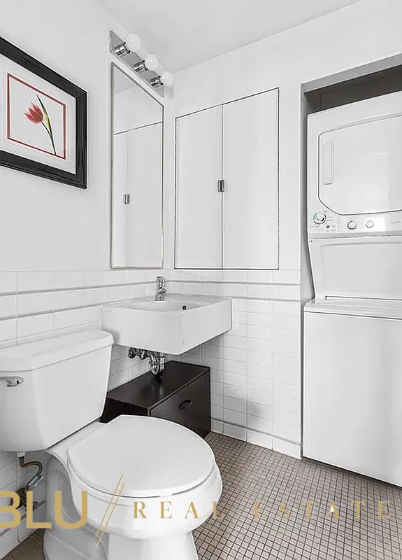 half bathroom featuring toilet, stacked washing maching and dryer, tile patterned floors, tile walls, and a sink