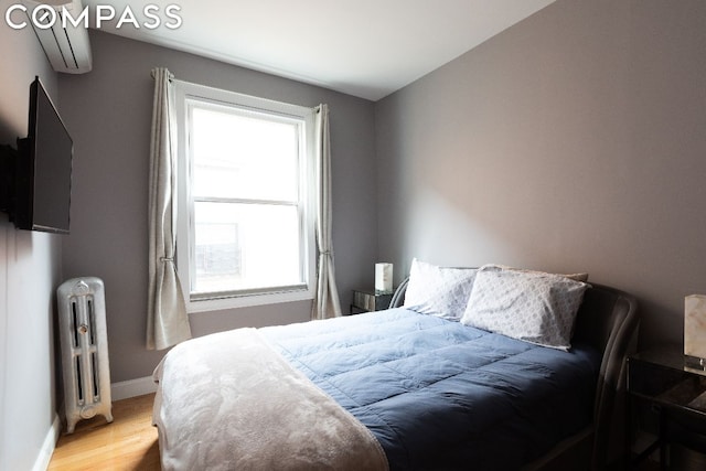 bedroom with a wall mounted air conditioner, radiator heating unit, multiple windows, and light hardwood / wood-style flooring