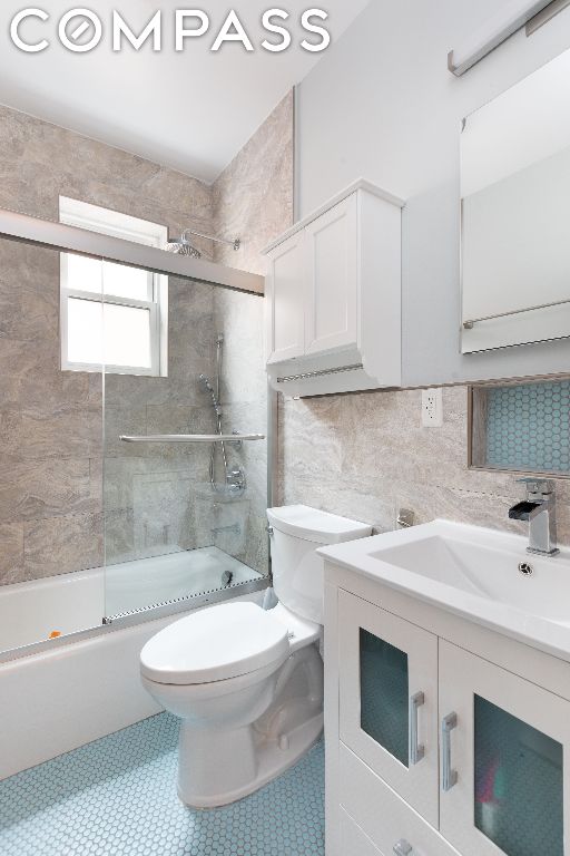 full bathroom featuring bath / shower combo with glass door, toilet, vanity, and tasteful backsplash