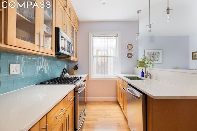 kitchen with appliances with stainless steel finishes, decorative light fixtures, light hardwood / wood-style floors, sink, and backsplash