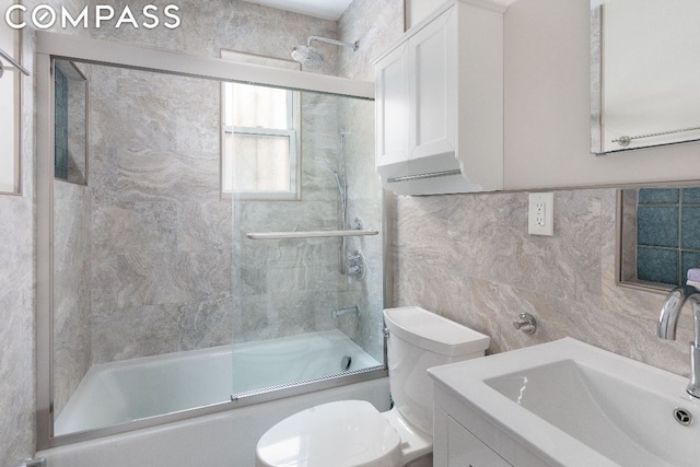 full bathroom featuring tile walls, combined bath / shower with glass door, vanity, and toilet