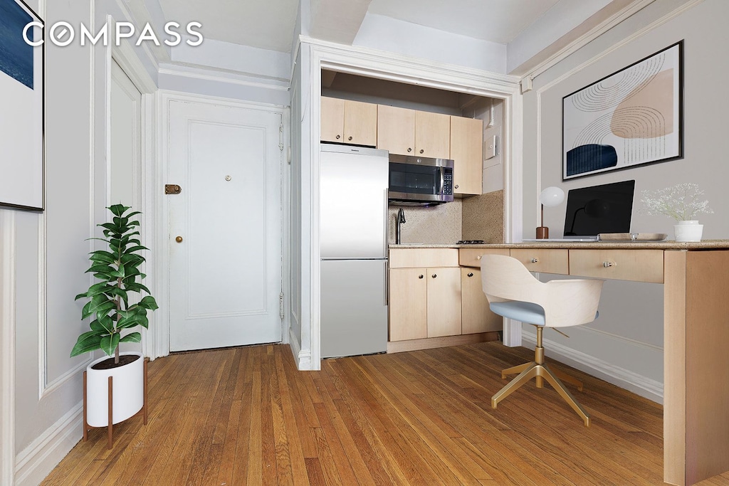 kitchen with light brown cabinetry, wood finished floors, stainless steel microwave, and fridge