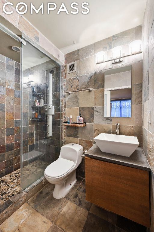 bathroom featuring toilet, vanity, tile walls, and a tile shower