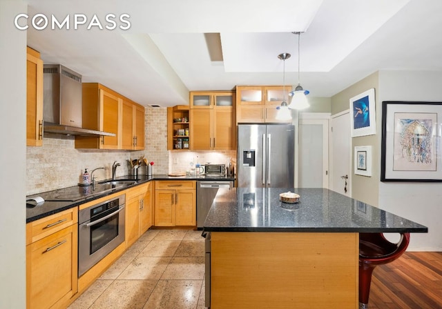 kitchen featuring a center island, appliances with stainless steel finishes, decorative backsplash, wall chimney exhaust hood, and a raised ceiling