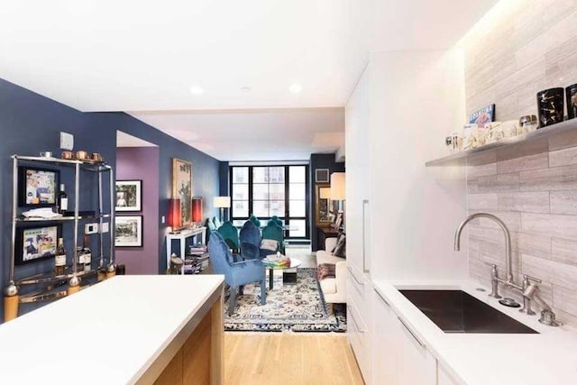 kitchen with white cabinets, light hardwood / wood-style flooring, sink, and tasteful backsplash