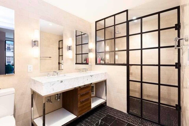 full bathroom with toilet, a sink, double vanity, and tile walls