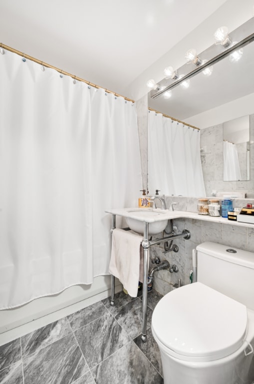 full bathroom featuring shower / bath combination with curtain, toilet, sink, and tile walls