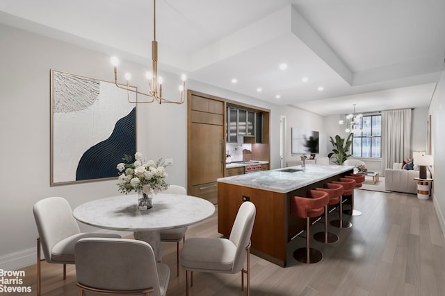 kitchen with an island with sink, hanging light fixtures, dark hardwood / wood-style flooring, an inviting chandelier, and a raised ceiling