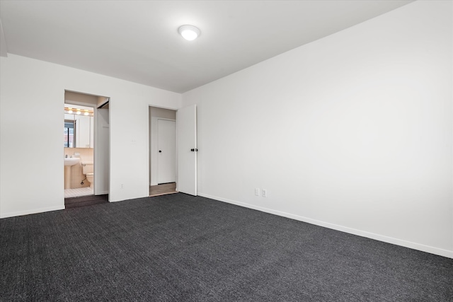 unfurnished bedroom featuring ensuite bathroom, baseboards, and dark carpet