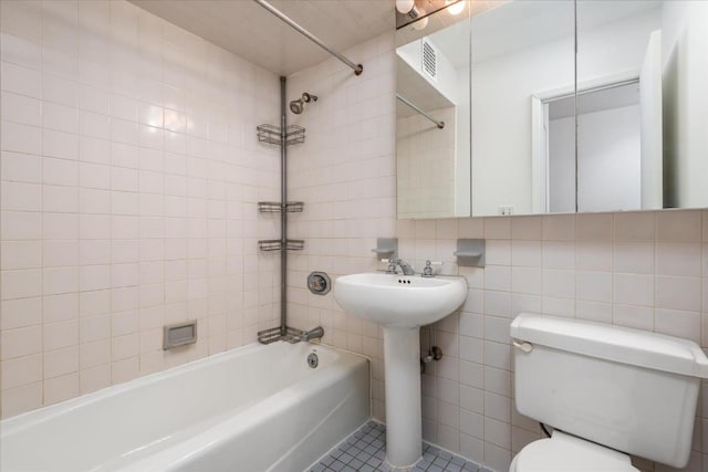 bathroom with toilet, tiled shower / bath, tile walls, and tile patterned floors