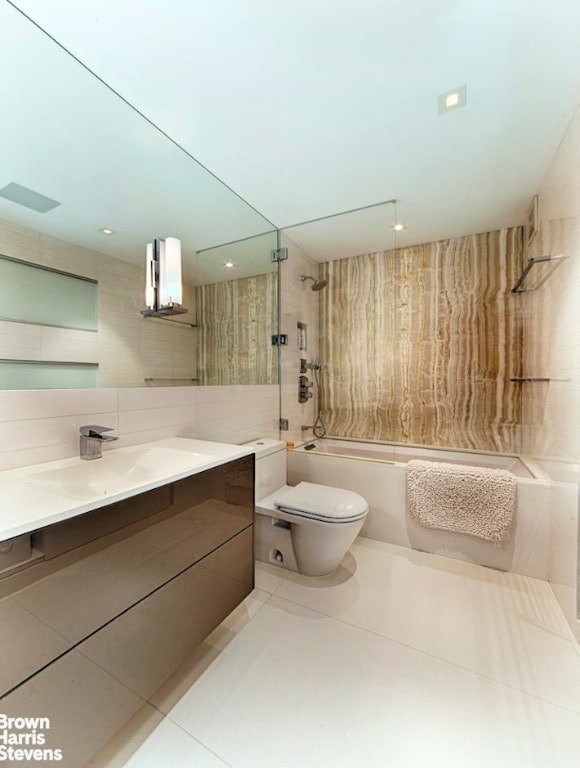 full bathroom featuring toilet, tiled shower / bath, tile walls, vanity, and tile patterned flooring