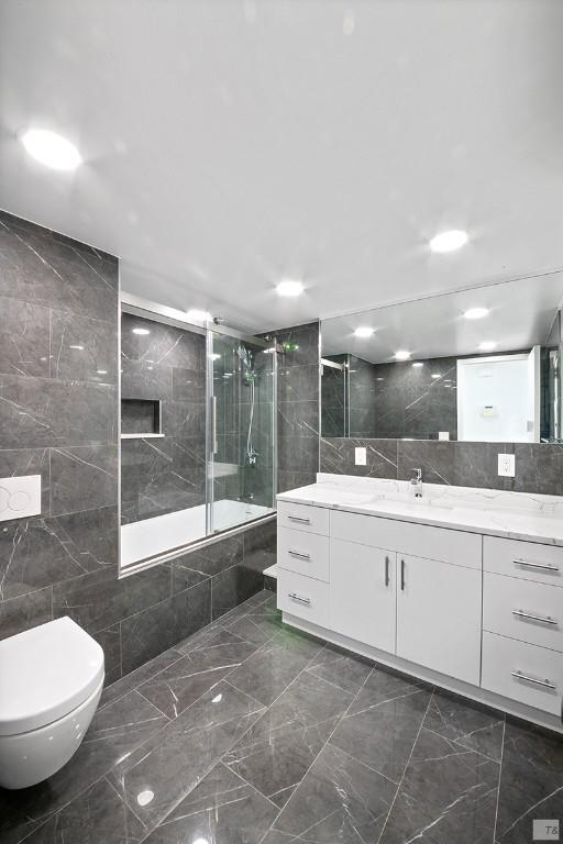 full bathroom with toilet, vanity, bath / shower combo with glass door, and tile walls