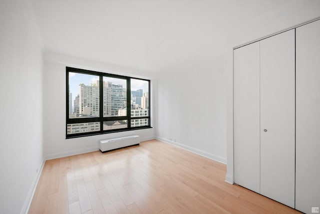 unfurnished bedroom with light hardwood / wood-style flooring, a closet, and a baseboard radiator