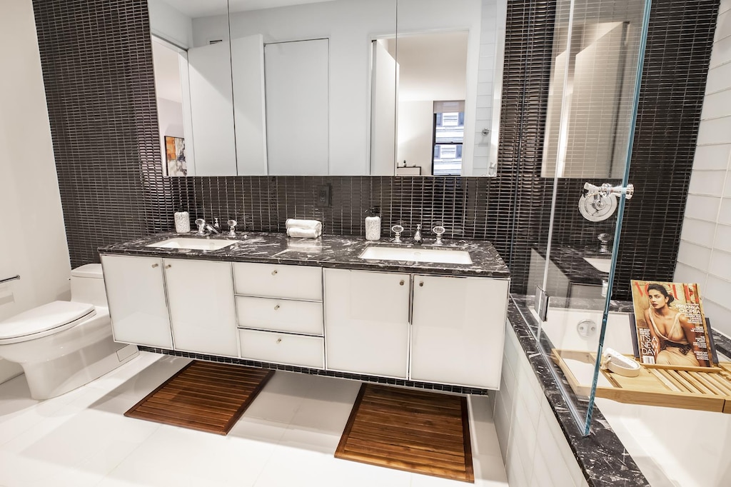 bathroom featuring toilet, tiled shower, a tub to relax in, double vanity, and tasteful backsplash