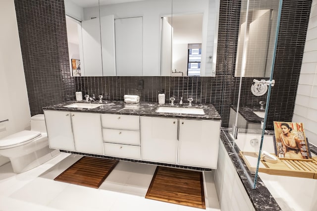 bathroom featuring toilet, tiled shower, a tub to relax in, double vanity, and tasteful backsplash